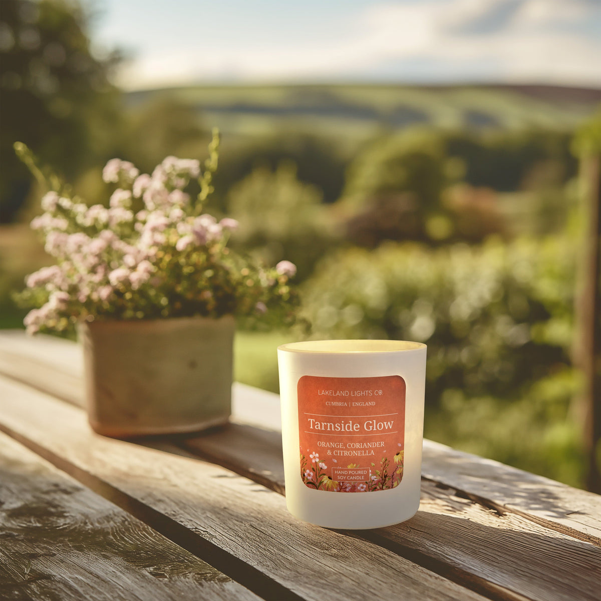 Tarnside Glow soy candle by Lakeland Lights, featuring orange, coriander, and citronella scent outside in a summer garden setting